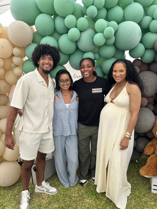 Baby shower hosts and guests smiling with a Visionary Grinders team member in front of a green and cream balloon arch